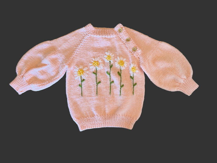 Pink knitted sweater with floral embroidery on a wooden surface