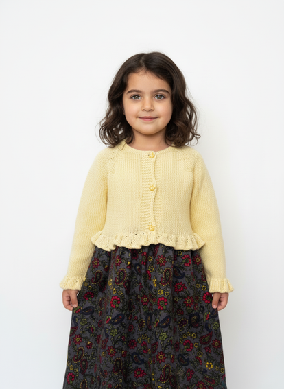 Young girl wearing a yellow cardigan and patterned skirt on a white background

